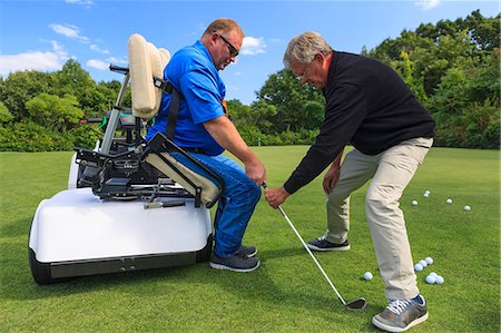 Man with a spinal cord injury in an adaptive cart at golf putting green with an instructor Stock Photo - Premium Royalty-Free, Code: 6105-08211340