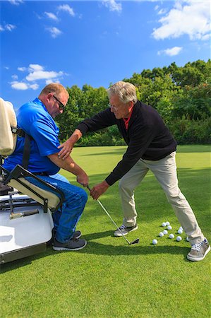 Man with a spinal cord injury in an adaptive cart at golf putting green with an instructor Stock Photo - Premium Royalty-Free, Code: 6105-08211339