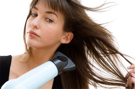 Portrait of a young woman using a hair drier Stock Photo - Premium Royalty-Free, Code: 6108-05855835