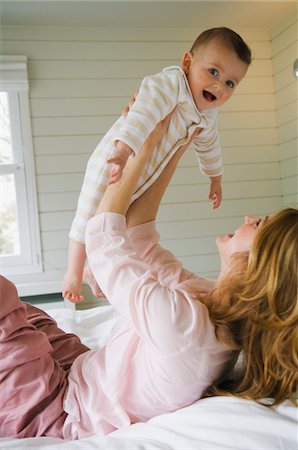 profile looking at hand - Young woman lying on the bed,  holding her baby, laughing Stock Photo - Premium Royalty-Free, Code: 6108-05855985