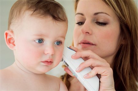 Mère de prendre la température de son bébé avec un thermomètre auriculaire Photographie de stock - Premium Libres de Droits, Code: 6108-05856008