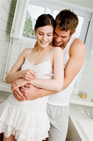 simsearch:6108-05856208,k - Smiling couple embracing in bathroom, looking at pregnancy test Fotografie stock - Premium Royalty-Free, Codice: 6108-05856146