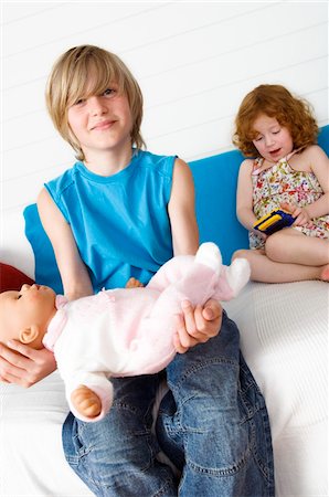 2 children at home, boy holding doll, girl playing video game Foto de stock - Sin royalties Premium, Código: 6108-05856133