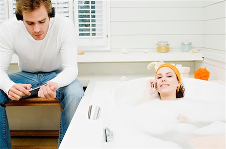 Couple in bathroom, woman phoning in bath, man with headphones filing his nails Stock Photo - Premium Royalty-Free, Code: 6108-05856209