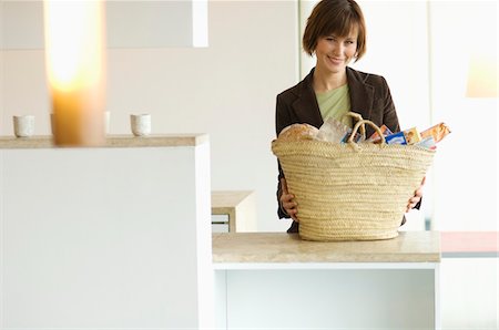 simsearch:6108-05856340,k - Young smiling woman with shopping basket in the kitchen Stock Photo - Premium Royalty-Free, Code: 6108-05856317