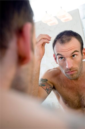 simsearch:6108-05856548,k - Tattooed man, barechested, looking in bathroom mirror Foto de stock - Sin royalties Premium, Código: 6108-05856546