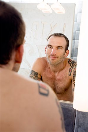 simsearch:6108-05856541,k - Tattooed man, barechested, looking in bathroom mirror Fotografie stock - Premium Royalty-Free, Codice: 6108-05856550