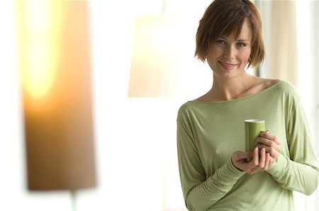 Young woman holding a cup, looking at the camera Stock Photo - Premium Royalty-Free, Code: 6108-05856510