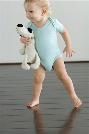 Little boy holding stuffed dog, standing on wooden floor Stock Photo - Premium Royalty-Free, Code: 6108-05856647