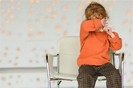 Little girl sitting on a chair, covering her face with her arm Stock Photo - Premium Royalty-Free, Code: 6108-05856696