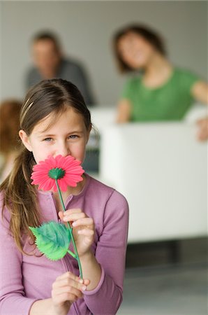 family modern - Little girl holding a plastic flower in front of her face, couple in the background Stock Photo - Premium Royalty-Free, Code: 6108-05856627