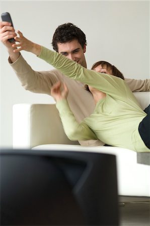 Couple lying on a sofa, watching TV, fighting over remote-control Stock Photo - Premium Royalty-Free, Code: 6108-05856737