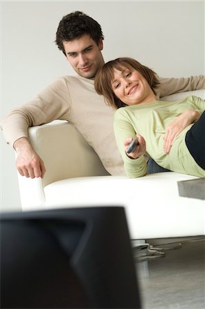 Smiling couple lying on a sofa, watching TV Stock Photo - Premium Royalty-Free, Code: 6108-05856735