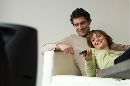 Smiling couple lying on a sofa, watching TV Stock Photo - Premium Royalty-Free, Code: 6108-05856736