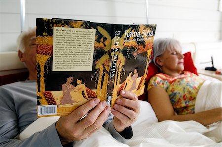 simsearch:6108-05856574,k - Senior couple in bed, woman sleeping, man reading Kama Sutra book Foto de stock - Sin royalties Premium, Código: 6108-05856884