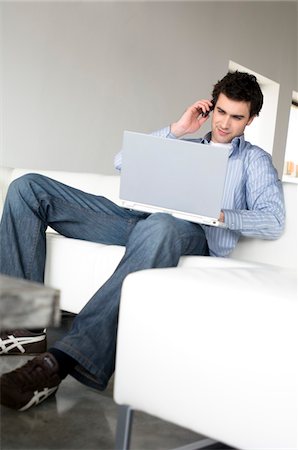 simsearch:6108-05858781,k - Man sitting on a sofa, using laptop computer and mobile phone Stock Photo - Premium Royalty-Free, Code: 6108-05856828