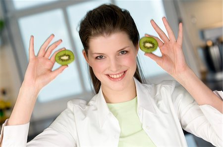 simsearch:6108-05856936,k - Portrait of a young smiling woman holding 2 halves of kiwi fruit Fotografie stock - Premium Royalty-Free, Codice: 6108-05856964