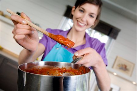 spoon in woman hand - Young smiling woman cooking tomato sauce Stock Photo - Premium Royalty-Free, Code: 6108-05857042