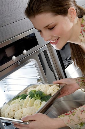 Young smiling woman putting broccolis and cauliflowers into an oven Stock Photo - Premium Royalty-Free, Code: 6108-05857069