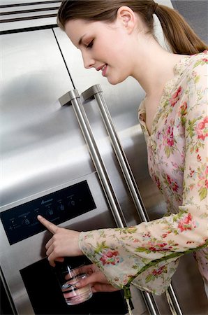 refrigerator - Young woman pouring water from a refrigerator water dispenser into a glass Foto de stock - Sin royalties Premium, Código: 6108-05857000