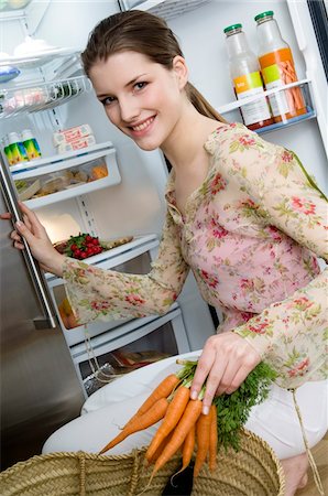 Young smiling woman filling refrigerator, holding carrots Stock Photo - Premium Royalty-Free, Code: 6108-05857015