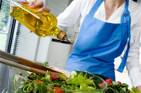 female kitchen aprons - Woman pouring olive oil into a salad, close-up Stock Photo - Premium Royalty-Free, Code: 6108-05857029