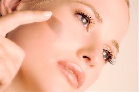 foundation cosmetics - Woman putting make-up base on her cheek, close-up, indoors (studio) Stock Photo - Premium Royalty-Free, Code: 6108-05857346