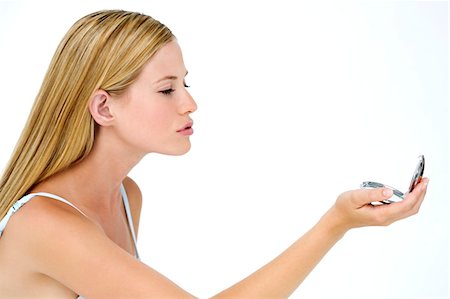 Portrait of a young woman looking at herself in a little miror, indoors (studio) Stock Photo - Premium Royalty-Free, Code: 6108-05857348
