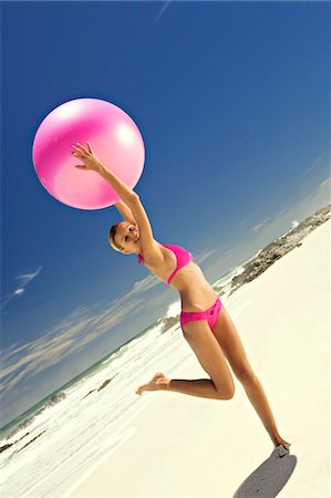 simsearch:6108-05859133,k - Young smiling woman in pink bikini on the beach, lifting a large ball Foto de stock - Sin royalties Premium, Código: 6108-05857611