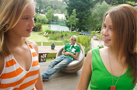 simsearch:6108-05857790,k - 2 teenage girls looking at each other on a terrace, teenage boy sitting in background Stock Photo - Premium Royalty-Free, Code: 6108-05857785