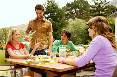 simsearch:6108-05858214,k - 2 young smiling couples sitting at garden table, man pouring wine Stock Photo - Premium Royalty-Free, Code: 6108-05857828