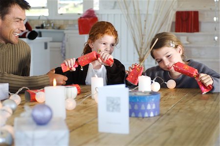 photos of christmas day living rooms - Ma  ad two children sitting around table, exchanging Christmas presents, indoors Stock Photo - Premium Royalty-Free, Code: 6108-05858055