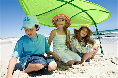 Three brother and sisters sitting on the beach, smiling, under a great green leaf, outdoors Foto de stock - Sin royalties Premium, Código: 6108-05858091