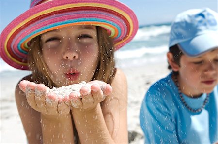 Portrait of a little girl blowing sand in her hands, boy in background, outdoors Stock Photo - Premium Royalty-Free, Code: 6108-05858098