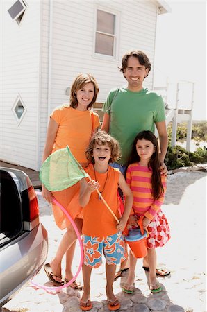 partir en voyage - Parents et deux enfants devant une maison, tenant des accessoires de plage, en plein air Photographie de stock - Premium Libres de Droits, Code: 6108-05858099