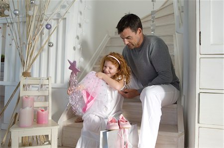 Father and daughter opening Christmas presents, girl holding a princess costume, indoors Stock Photo - Premium Royalty-Free, Code: 6108-05858007