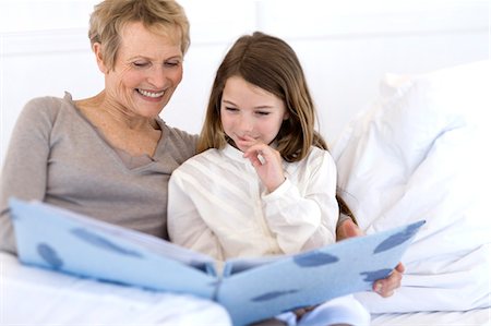 Senior woman and little girl in bed, looking at photograph album Stock Photo - Premium Royalty-Free, Code: 6108-05858148