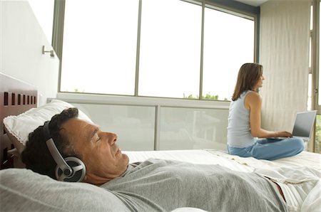 simsearch:6108-05873527,k - Couple in bedroom, man listening to music, woman using laptop, indoors Stock Photo - Premium Royalty-Free, Code: 6108-05858275