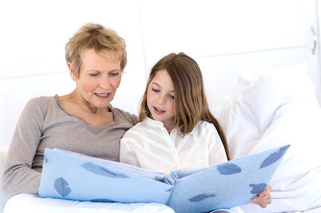 Senior woman and little girl in bed, looking at photograph album Stock Photo - Premium Royalty-Free, Code: 6108-05858200