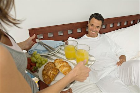 Woman bringing breakfast to man lying on bed, indoors Stock Photo - Premium Royalty-Free, Code: 6108-05858300