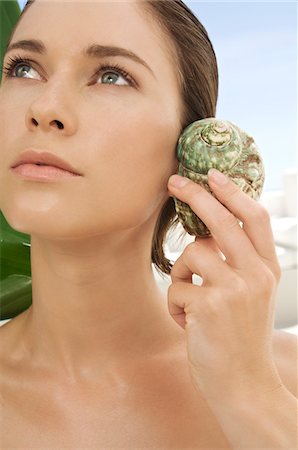 simsearch:6108-05857534,k - Portrait of a young woman holding a shell against her ear, outdoors Fotografie stock - Premium Royalty-Free, Codice: 6108-05858474