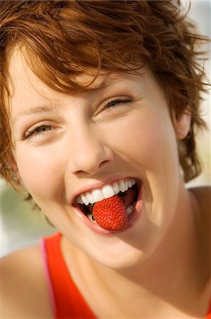 Portrait of a young woman holding strawberry between her teeth Stock Photo - Premium Royalty-Free, Code: 6108-05858512