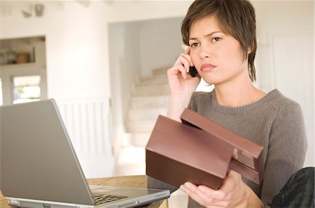 e-commerce - Young woman with laptop, phoning, holding box Stock Photo - Premium Royalty-Free, Code: 6108-05858698