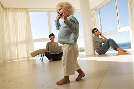 Little girl using mobile phone, parents in background Stock Photo - Premium Royalty-Free, Code: 6108-05858611