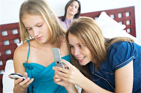 2 souriant des adolescentes à l'aide de téléphones mobiles, femme en arrière-plan Photographie de stock - Premium Libres de Droits, Code: 6108-05858627