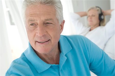 Couple in bedroom, portrait of man, woman listening to music with headphones in background Stock Photo - Premium Royalty-Free, Code: 6108-05858755