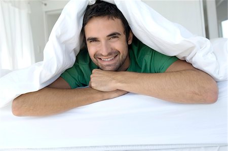 simsearch:6108-05873527,k - Young smiling man lying under duvet Stock Photo - Premium Royalty-Free, Code: 6108-05859055