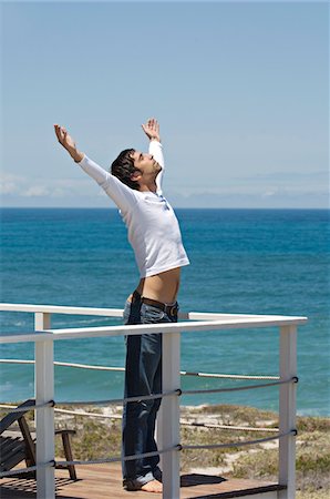 Young man stretching on terrace, sea in background Stock Photo - Premium Royalty-Free, Code: 6108-05859058