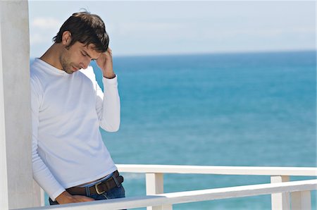 sad face and adult - Young thinking man leaning against wall on a terrace, sea in background Stock Photo - Premium Royalty-Free, Code: 6108-05859068