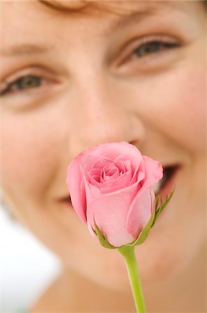 Portrait of young smiling woman with rose in front of face Stock Photo - Premium Royalty-Free, Code: 6108-05859120